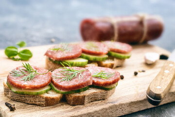 rye bread sandwich with smoked sausage salami dill and cucumber on cutting board, close-up