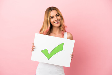 Young woman over isolated pink background holding a placard with text Green check mark icon with happy expression