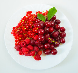 Assorted red fresh berries on a plate on a white background.