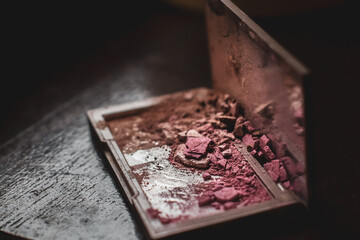 a close up on a smashed make up product, bronzer and blush, all shattered in pieces of dust and product, 