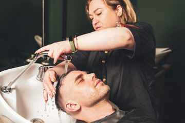 Naklejka premium Hairdressing, girl hairdresser washes the head of a young guy in a barbershop