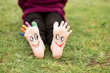 Naklejka premium Close up of child human pair of feet painted with smiles outdoor in sunny park