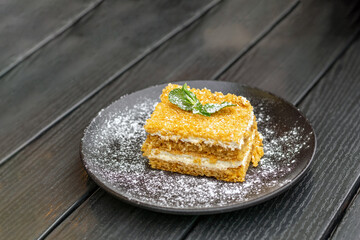 A piece of honey cake with butter cream, garnished with powdered sugar and mint.