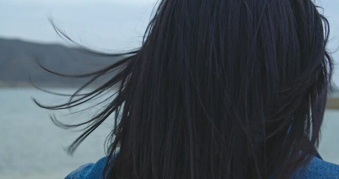 Young woman with jeans jacket and black  hair walks  on the empty sandy beach  