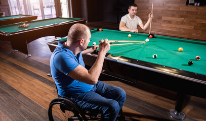 Adult men with disabilities in a wheelchair play billiards in the club