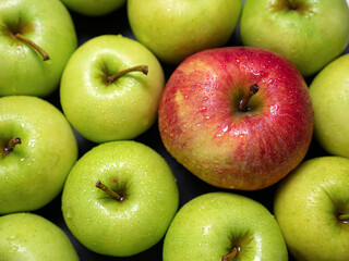 One red and many green apples rotating, closeup