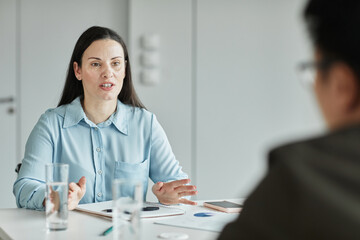 Portrait of empowered businesswoman talking to colleagues during meeting in office, copy space