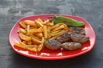 meatballs and potatoes on a red plate on black background