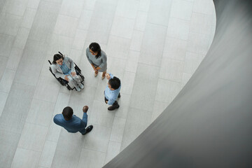Graphic top down view at young businesswoman in wheelchair talking to diverse group of people in...