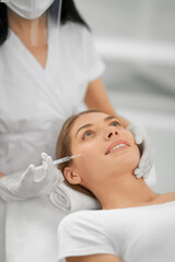 Close up of smiling young brunette woman on procedure injection anti-aging skin in beautician. Concept of process injection for improve the condition face. 