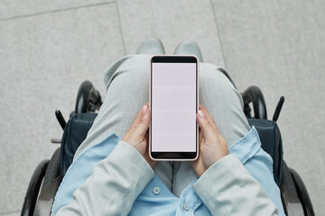 Minimal top view closeup of unrecognizable woman in wheelchair holding smartphone with blank white...