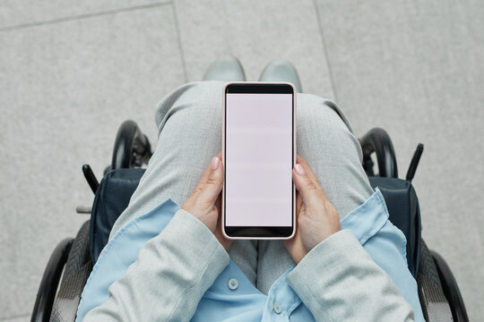 Minimal top view closeup of unrecognizable woman in wheelchair holding smartphone with blank white screen, mobile app concept, copy space