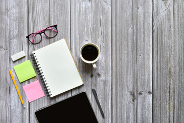 Still life, business or office supplied concept, Top view image of open notebook with coffee cup pencil tablet and equipment with blank pages on old brown wooden background, for adding text