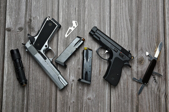 Still life of black and silver handgun with cartridge magazine, flashlight, small knife and multipurpose tool on old grungy brown wooden background, Black and silver semi-automatic with various tools