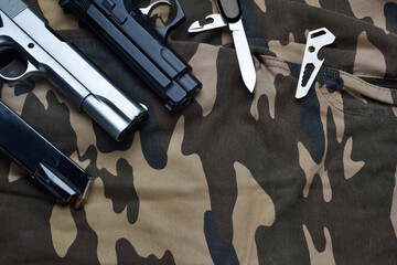 Still life of black and chrome handgun with cartridge magazine, small knife and multifunctional pocket tool on camouflage soldier pant, various tactical weapon and tools for defense