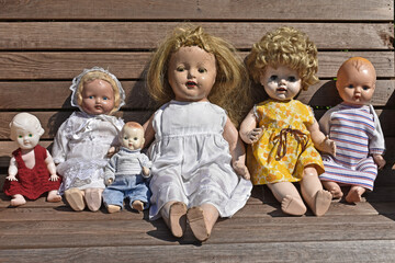 Closeup of a group of creepy old dolls sitting on a wooden bench