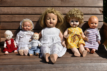 Closeup of a group of creepy old dolls sitting on a wooden bench