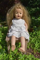 Vertical shot of a creepy old doll put on the chair in the garden