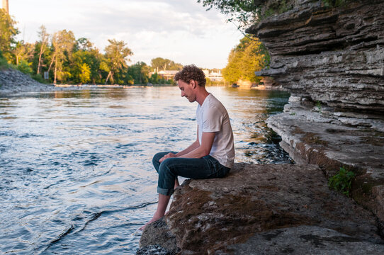 Man sits on the rocks by a river at sunset. 