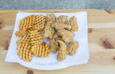 Plate of freshly cooked whiting fish nuggets and waffle fries placed on a paper towel.