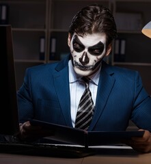 Businessman with scary face mask working late in office