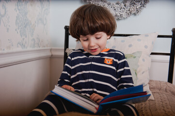 Little boy in pajamas reads a book before bedtime.