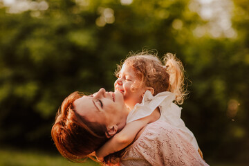 Cute little girl hugging her red haired young mom in the park. Happiness. 