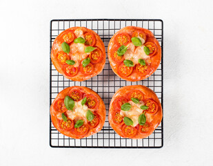 Children mini pizza pink with tomatoes, mozzarella and basil on a serving rack on a white background top view