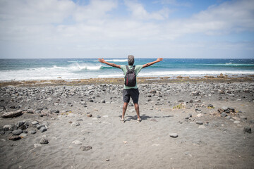 traveler boy at the beach opens his arms and looks at the sky, he is enjoying his trip and is happy. Traveler concept.