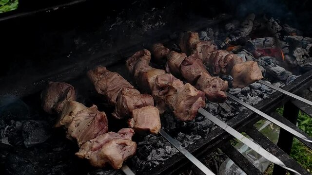 Meat on skewers. Close-up process of cooking yummy shashlik in nature. Delicious food on metal skewer in bbq. Pork at the stake. Roasted meat on the coals.