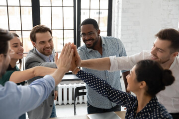 Excited millennial teammates joining hands for giving high fives. Team of happy employees...