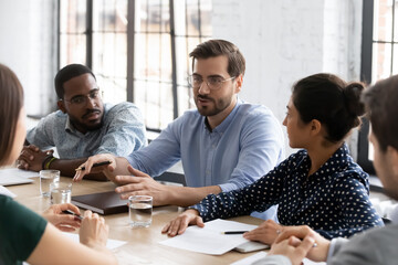 Satisfied millennial employee sharing ideas with diverse team on office brainstorming meeting,...