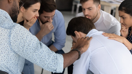 Depressed desperate man sharing bad news, problem, loss with team. Shocked diverse group sitting in circle, expressing solidarity and support to stressed mate. Therapy center mental health meeting