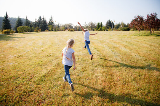 two girls cheerfully run and jump in the open space on the green grass. summer vacation concept