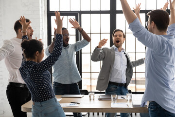 Happy excited millennial employees shouting for joy, raising hands for emotional high fives....