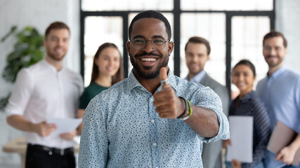 Portrait of happy African American male business leader making thumb up like gesture at camera....