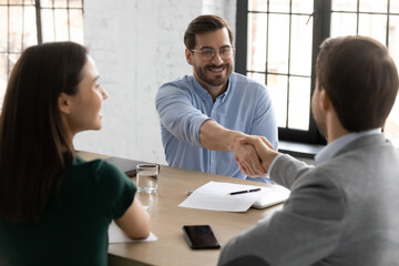 Happy employee candidate shaking hands with employer or recruiter on job interview. Couple consulting bank broker or lawyer, meeting with real estate agent for consultation, giving handshake