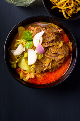 Northern Thai food (Khao soi), Spicy coconut milk curry egg noodles soup with beef in a bowl on black background, Top view