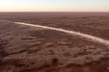 A roadtrain in far outback Queensland leaves a trail of bull dust along the road.