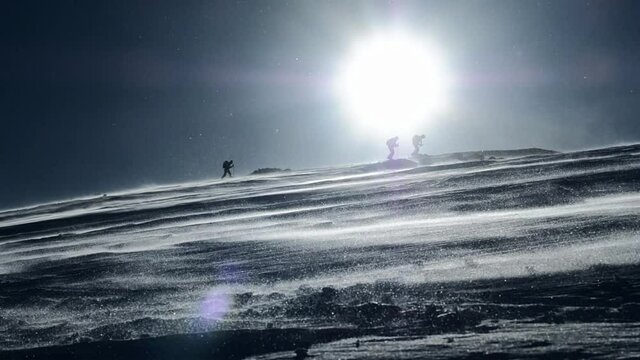 backcountry skiers ascending Mt. Schneibstein at Berchtesgaden national park in sunny but windy conditions, the wind blowing snow crystals all over the place