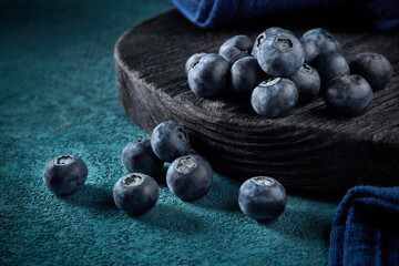 Ripe blueberries on black wooden board on dark blue background.