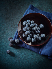 Ripe blueberries in saucer on dark blue background. Top view