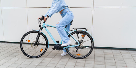 Naklejka premium Unrecognizable woman, no face shot, sitting on modern electric bicycle, white wall background 
