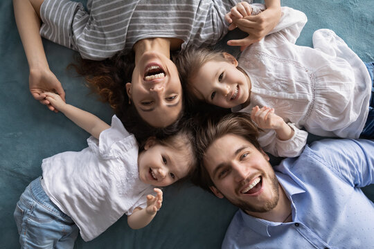 Close up top view portrait of smiling young parents have fun play with two little daughters at home. Happy Caucasian family with small girls children kids, enjoy family weekend. Parenthood concept.