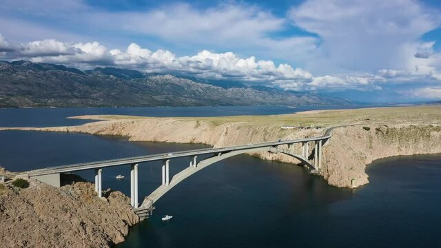 Paski Most - Boat Sailing Under Pag Bridge With Scenic Mountain View Under White Clouds In Croatia. - aerial