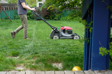 Man mowing tall grass; suburban back yard with deck and landscaping
