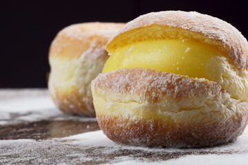 Berlin balls, known as Sonho in Brazil on wooden table with scattered icing sugar. It consists of a fried sweet dough filled with a cream and sugar on top. Selective focus.