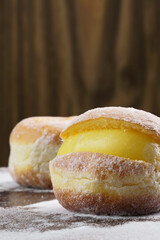 Berlin balls, known as Sonho in Brazil on wooden table with scattered icing sugar. It consists of a fried sweet dough filled with a cream and sugar on top. Selective focus. Vertical.