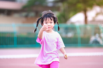 Cute 4 year old Asian girl running and having fun. Happy child was wearing a pink dress. Children braided two braids. Sweet smile kid.