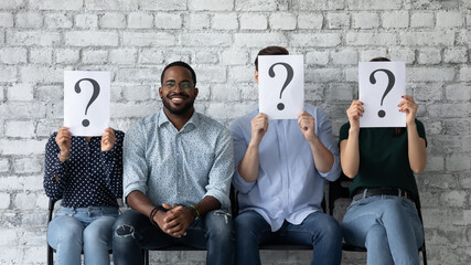 Happy job candidate celebrating successful interview, sitting near failed competitors, looking at camera, smiling. Black male applicant winning employment contest from seekers with hidden faces